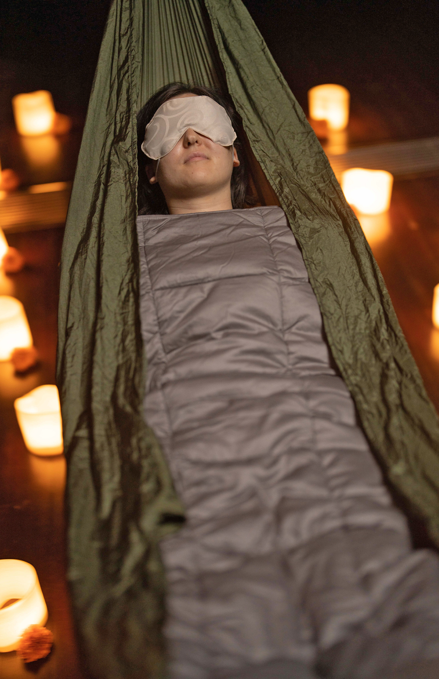 Woman sleeping in a hammock with a blanket and eye mask on surrounded by candles