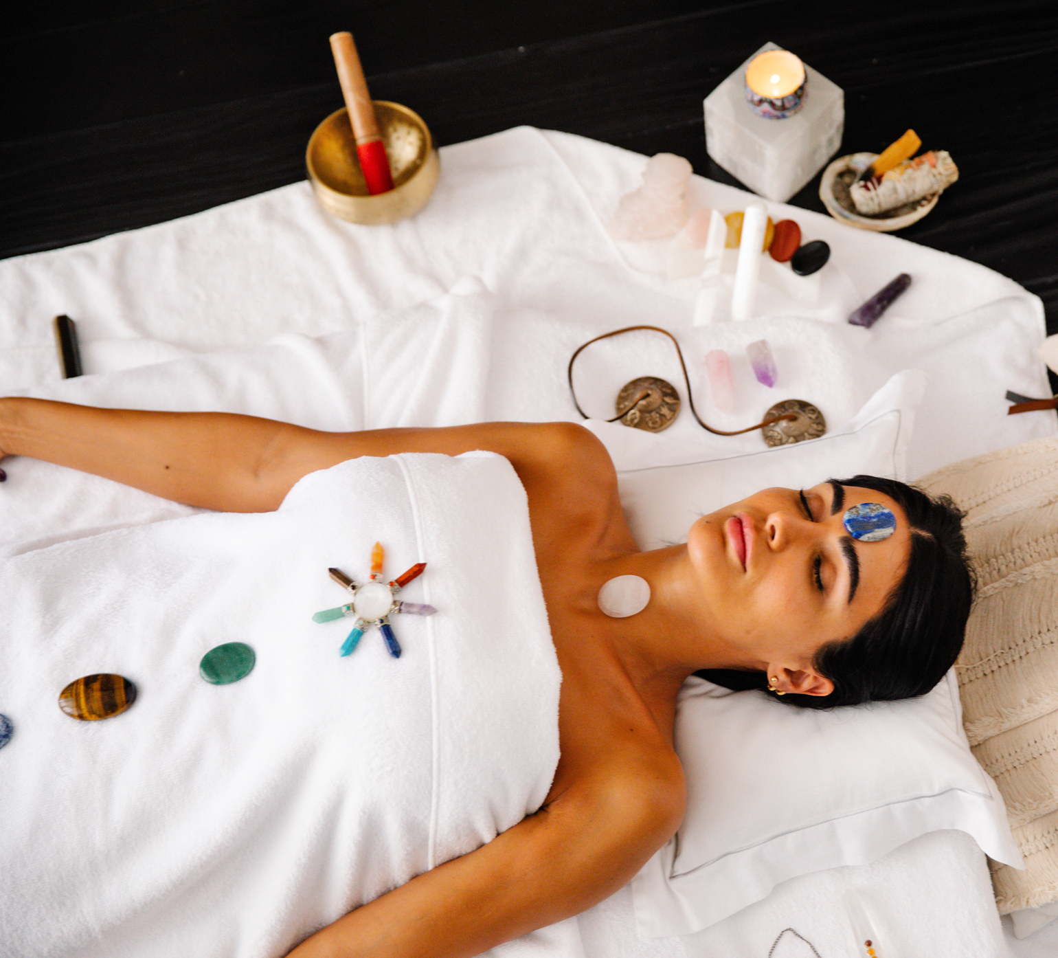 Woman lying down covered in a towel with stones on chest and stomach