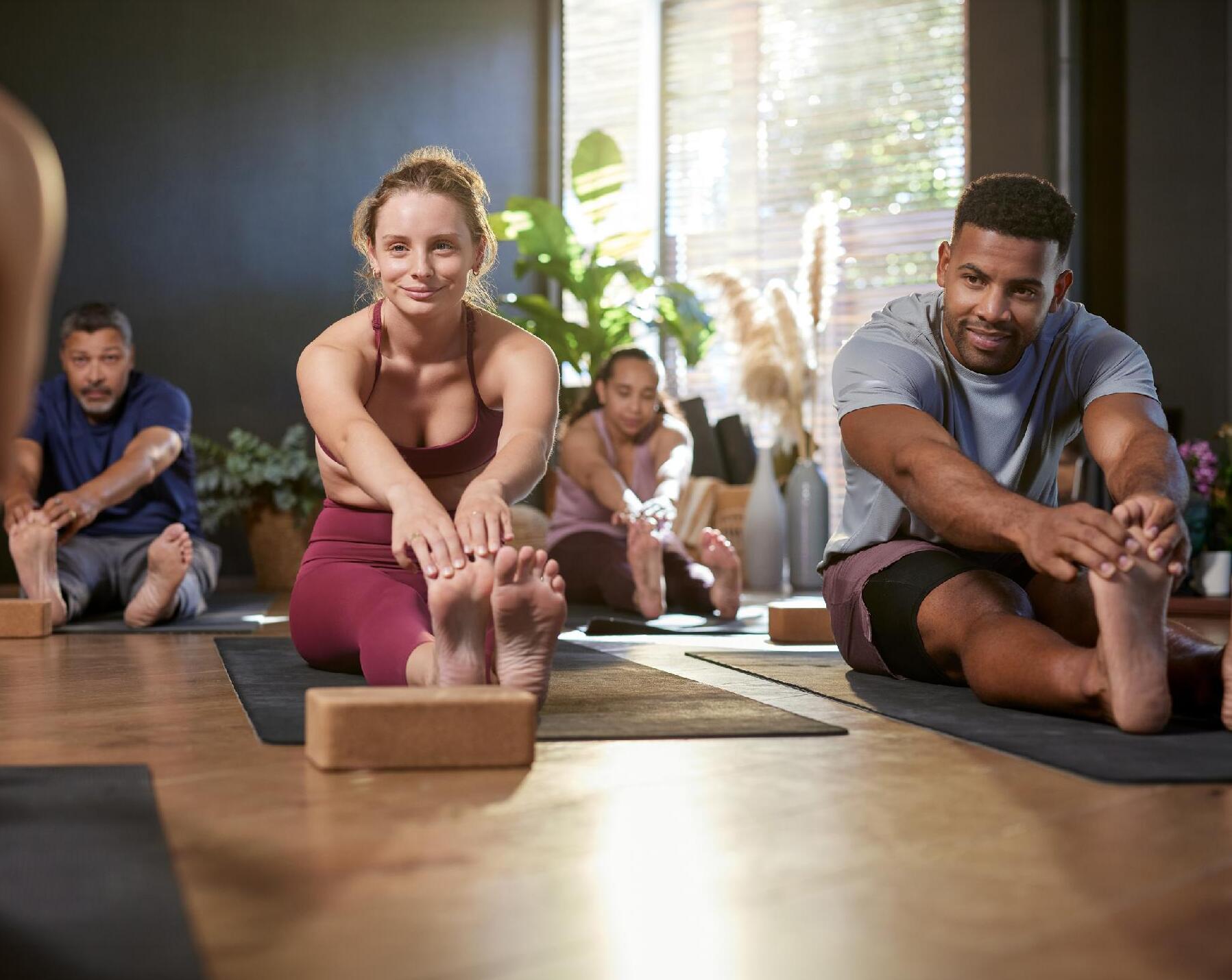 People stretching on mats in a yoga class on wooden studio floor