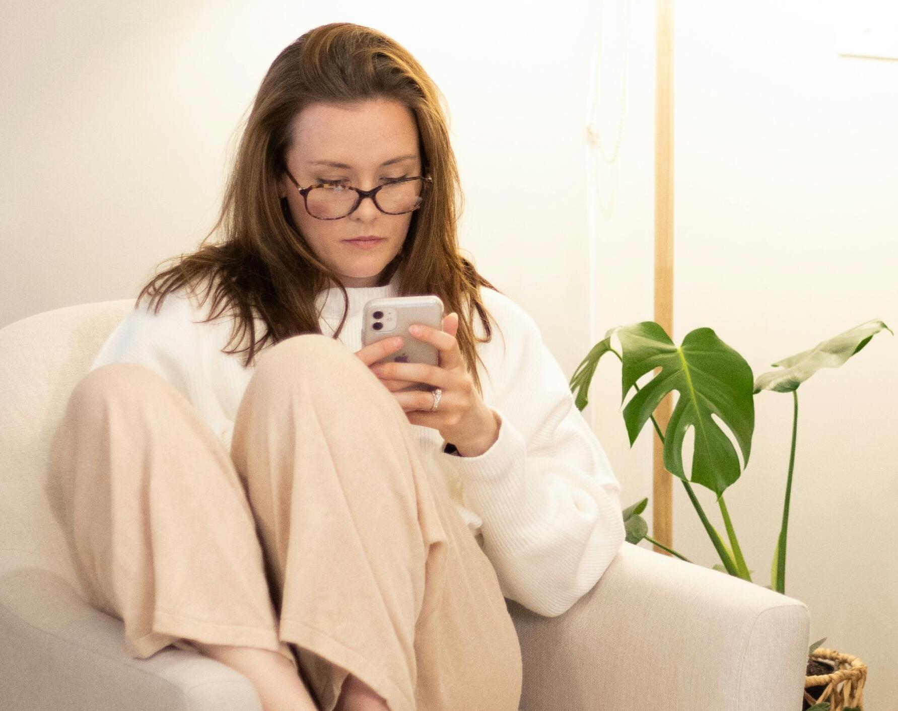 Woman, seated in armchair, looking at her phone