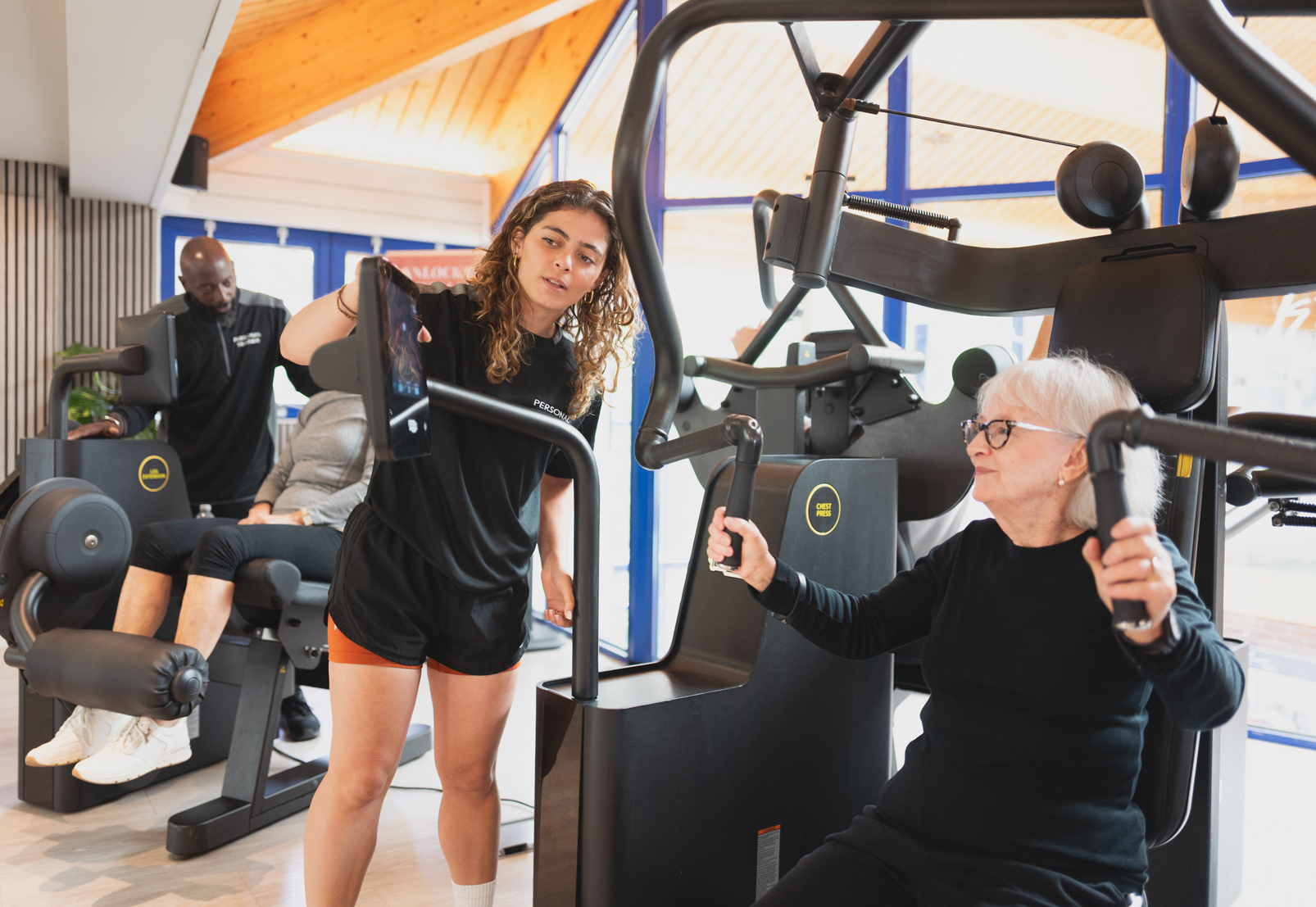 Young female personal trainer assists older woman using Technogym Biocircuit strength equipment at Colets Health and Fitness