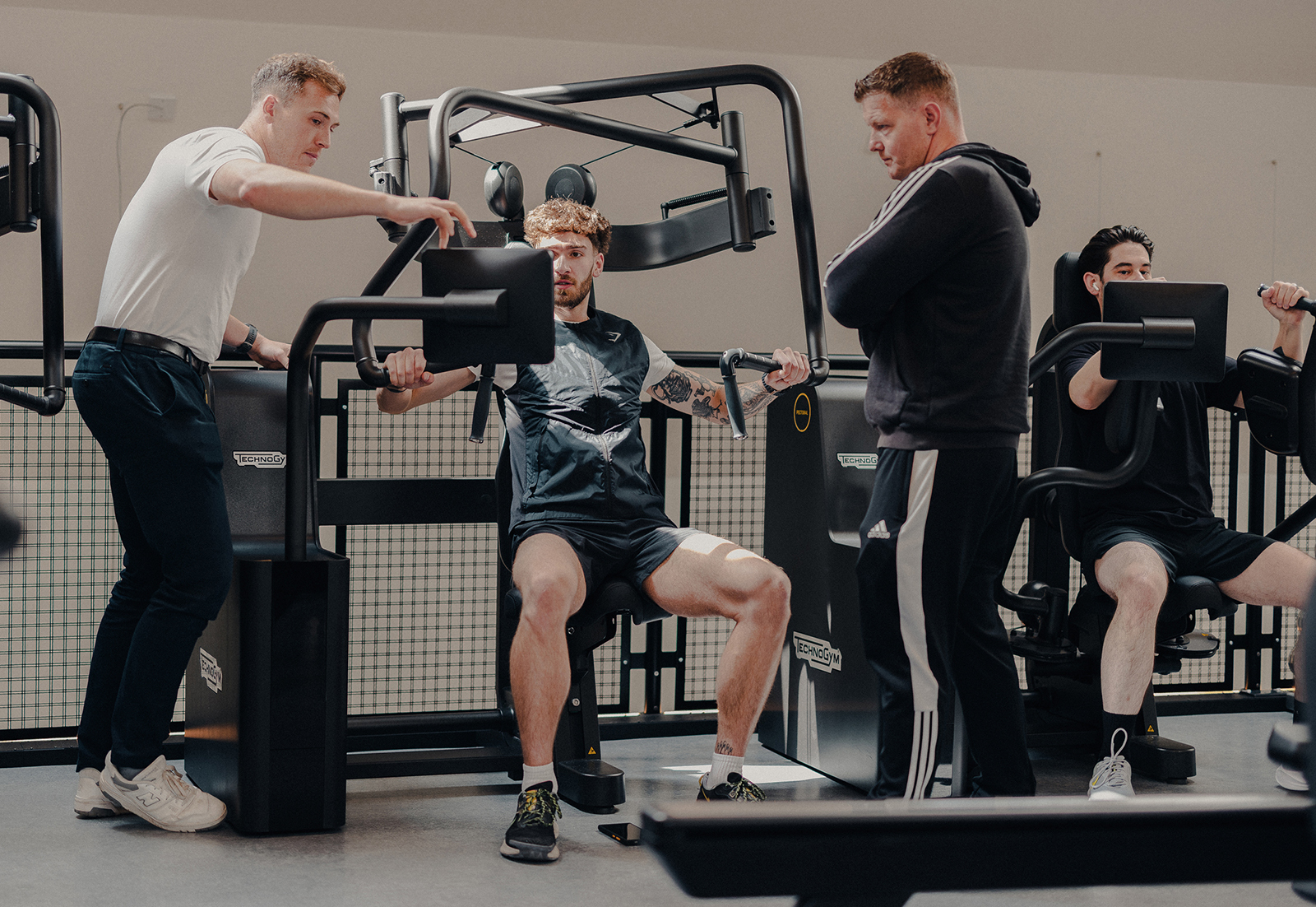 Male assists young man with Technogym Biocircuit equipment while another male looks on