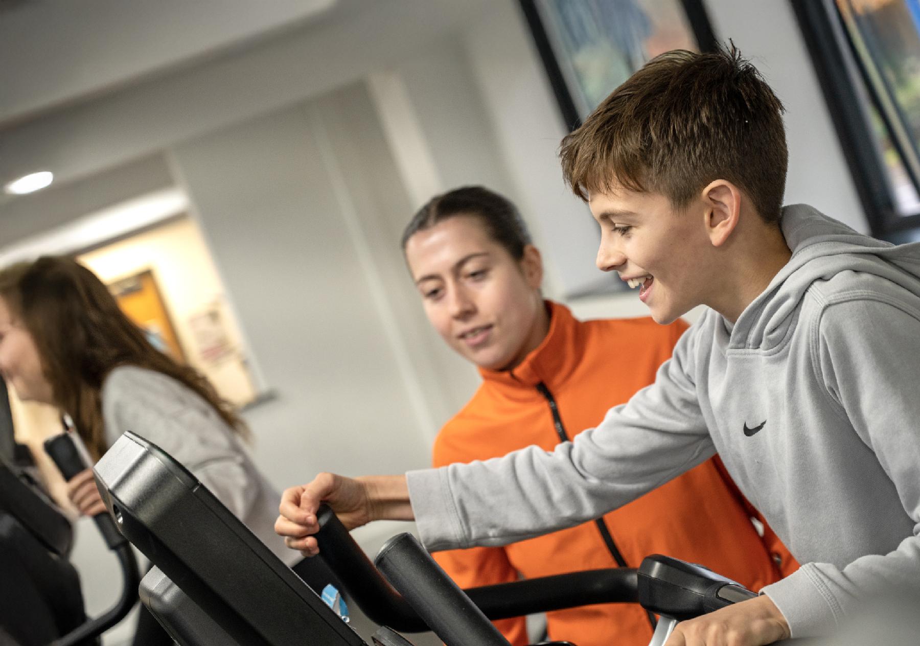 Boy using gym equipment with instructor watching