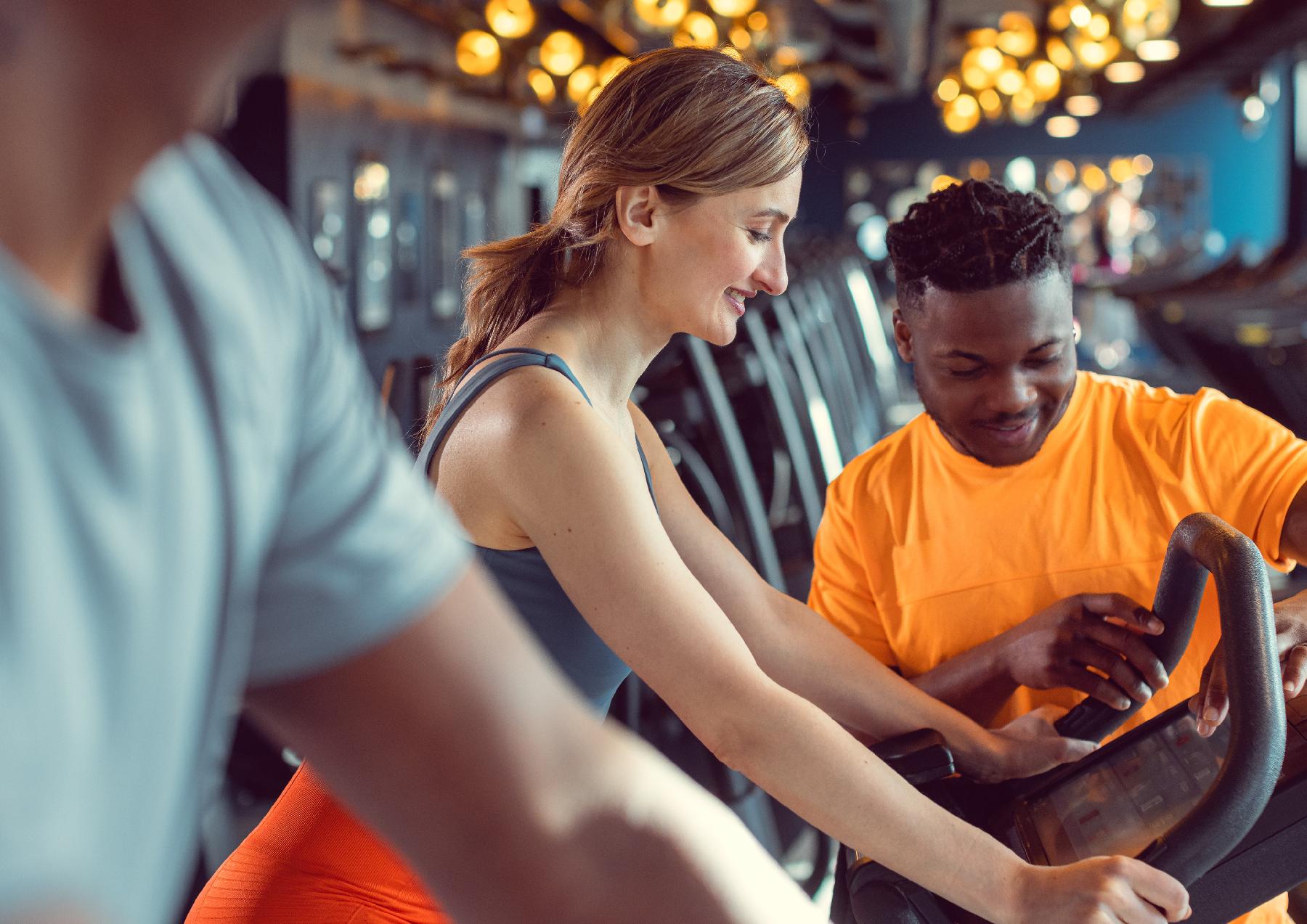 Woman using gym equipment with instructor looking on