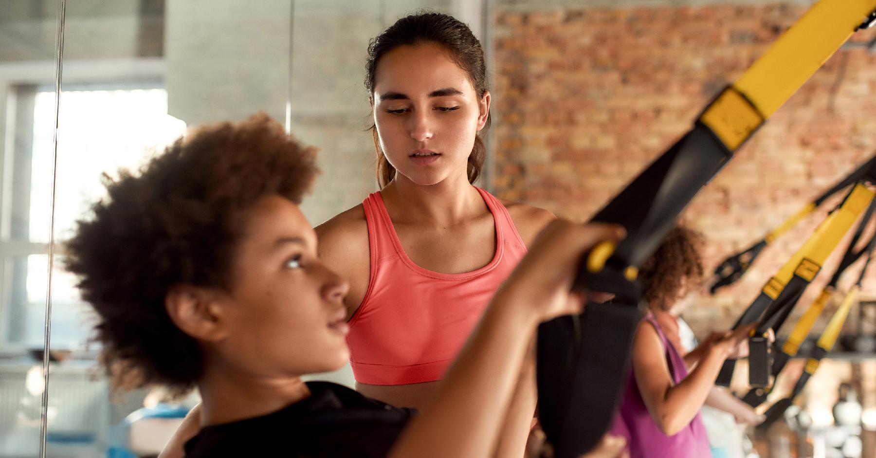Young person using gym equipment with instructor looking on