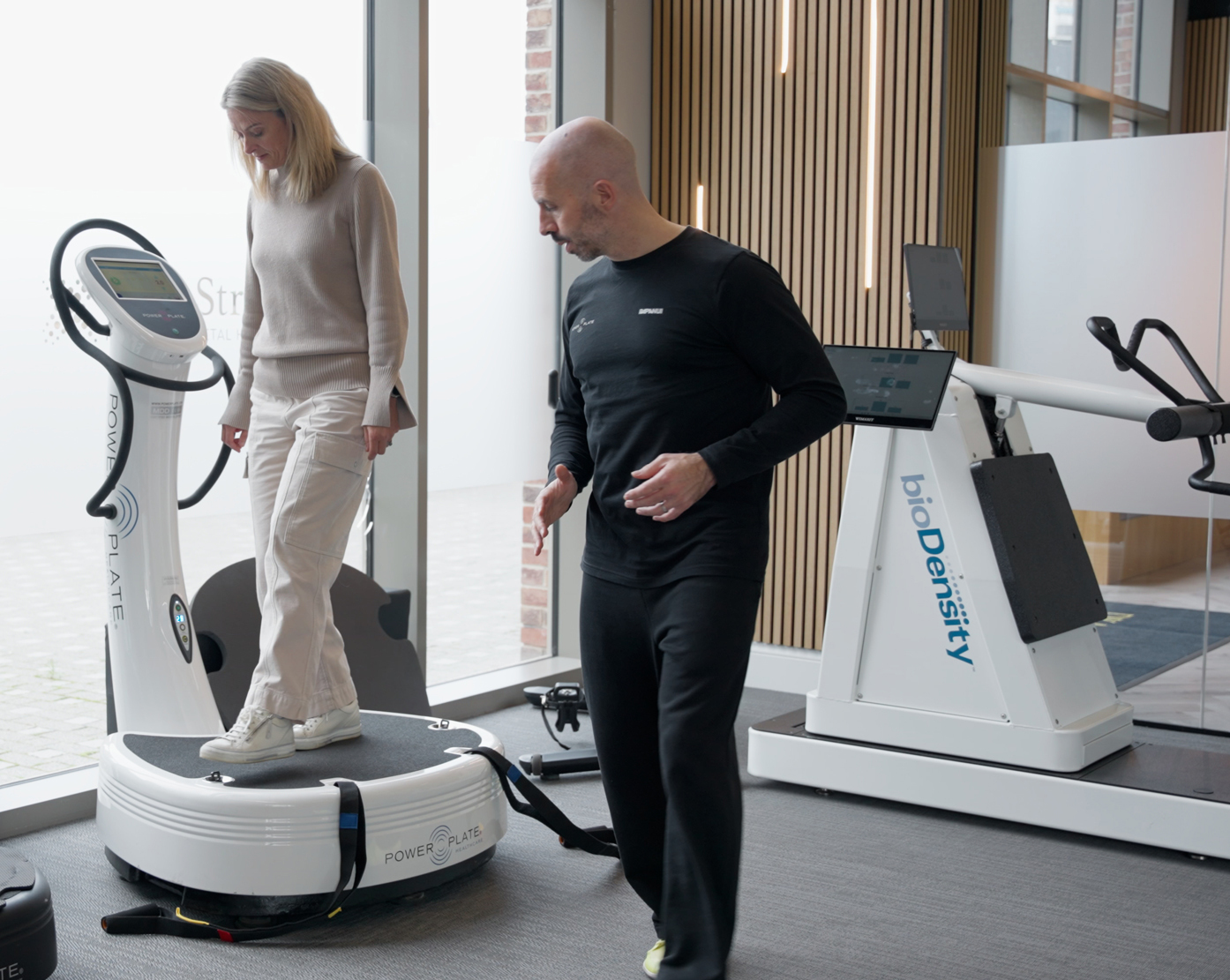 Woman using Powerplate equipment with instructor looking on