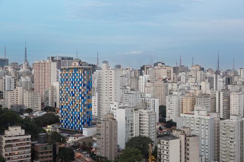 In the daytime, a coat of sheet metal creates a pixelated skin in blue, grey and gold