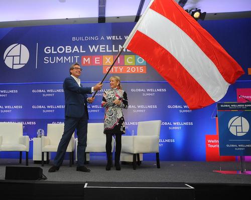 2016 Global Wellness Summit co-chair Franz Linzer waves the Austrian flag at last year's Summit while GWS CEO Susie Ellis looks on