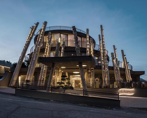 The architects have created a unified, rhythmically alternating facade from native larch tree trunks, which cover the old and new parts of the building / NOA*