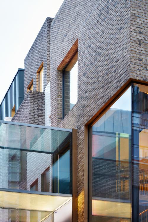 A double-height glazed bridge crossing the footpath at the first-floor level joins the two buildings / SODA Studio