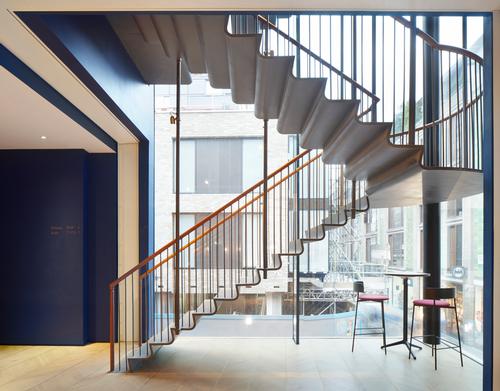 A rolled-steel feature staircase hangs in the glazed corner of one of the buildings / SODA Studio