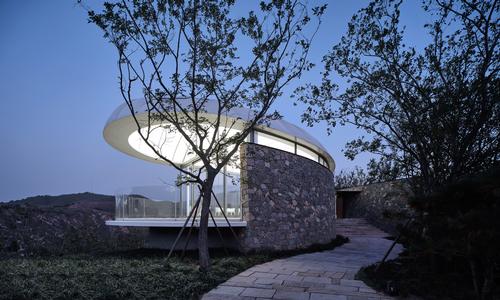The building is constructed on a stone plinth and has a stone wall running along one of its sides / zystudio