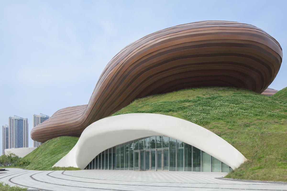 A glazed curtain wall built into the grassy hill conveys that the hill is a functional element of the design / Xia Zhi